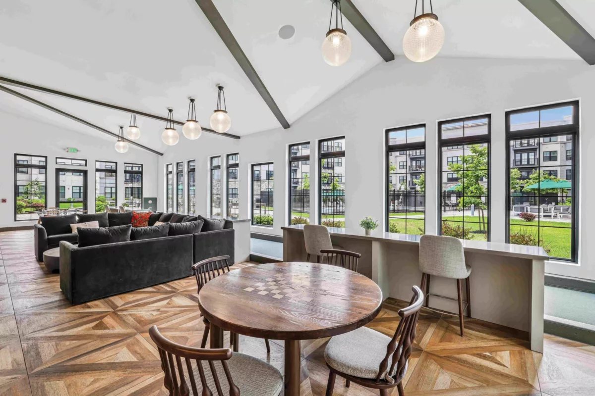 Game room with round table, black sofa, and floor-to-ceiling windows.