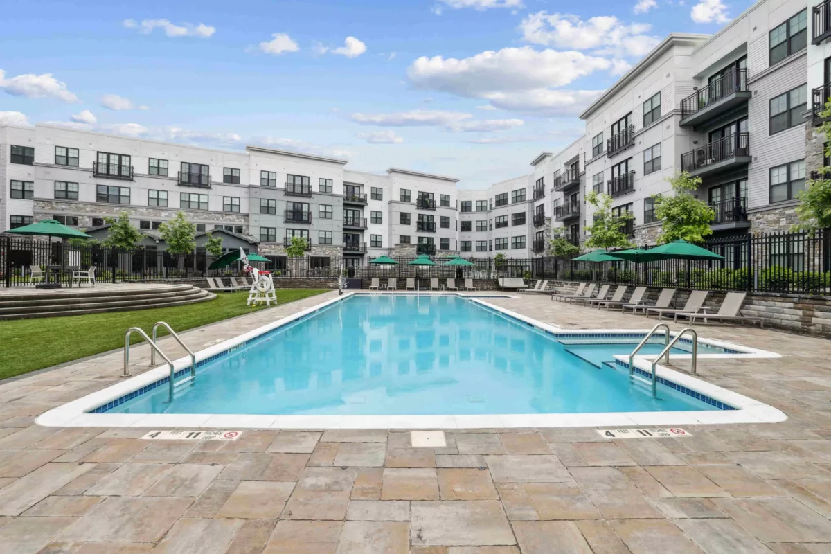 Outdoor swimming pool with lounge chairs, umbrellas, and apartment buildings.